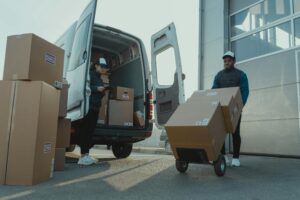 Fotobox Two couriers load boxes into a van for shipment, showcasing logistics and teamwork.